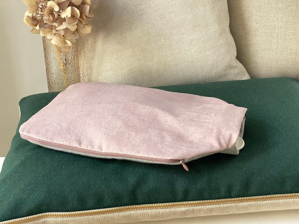 Hochwertiger Wärmflaschenbezug mit Wärmflasche. Bezug in rosa und grau mit Reißverschluss. Handgefertigt in Berlin. Liegt hier auf einem grünen Kissen von HETTI., im Hintergund eine Vase mit Trockenblume