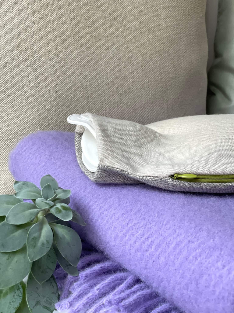 Hochwertiger Wärmflaschenbezug KAT, beige und graues Schurwoll-Leinen-Gemisch mit grünem Reißverschluss, elegant und schlicht, hier auf einer lila Wolldecke