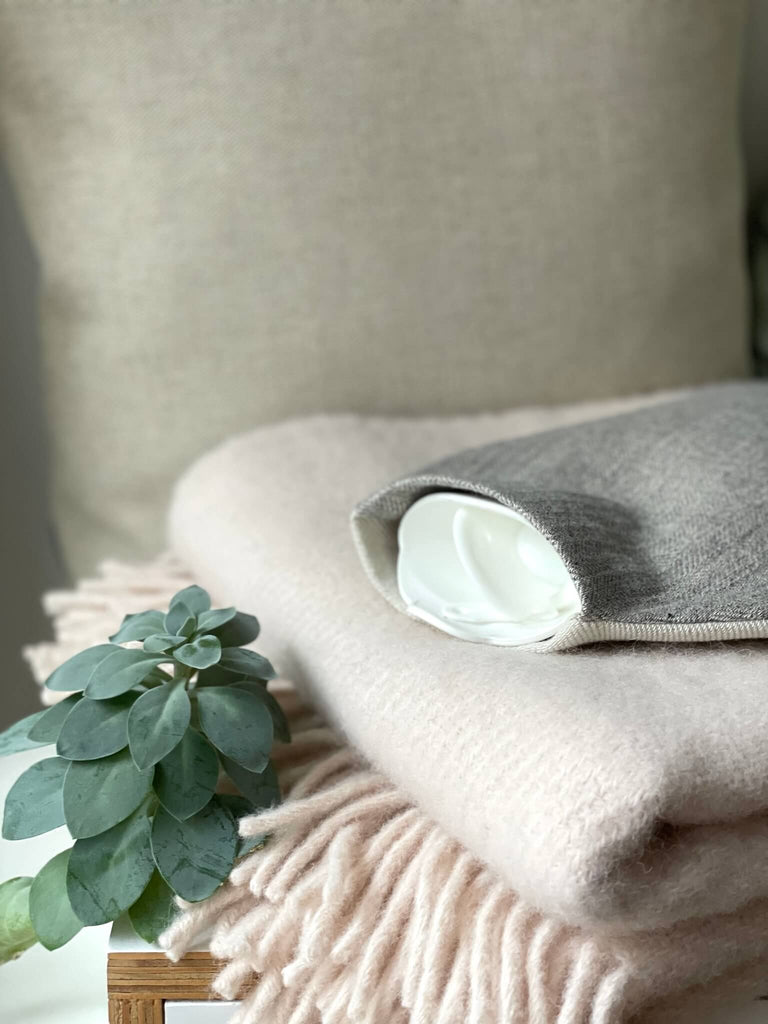 Schöne Wärmflasche in grau und beige auf einer weichen Wolldecke in rosé